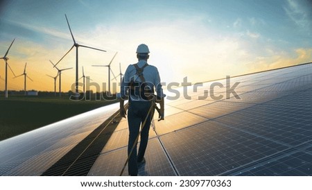 Professional Male Green Energy Engineer Walking On Solar Panel, Wearing Safety Belt And Hard Hat. Man Inspecting Sustainable Energy Farm With Wind Turbines. VFX Edit Visualizing Flow of Electricity. Royalty-Free Stock Photo #2309770363