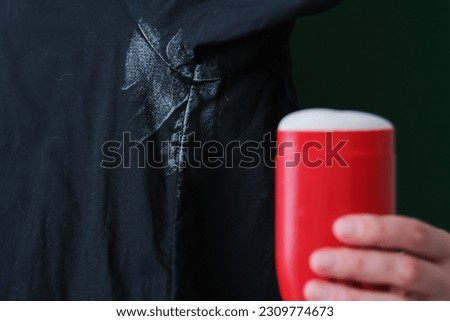 Deodorant stain on black shirt. on the background a hand holding a red deodorant. stick daily life stain concept. High quality photo
