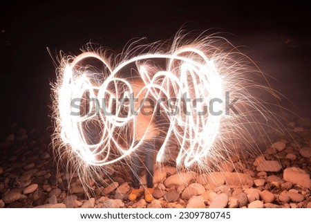 A child is playing with hand held fireworks on the riverbed at night.