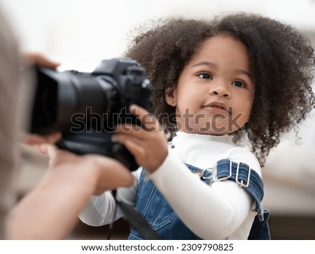 Cute kid playing digital camera learn to take picture. Afro hair multiracial girl interested in camera and lens to be adorable photographer. Cheerful little child holding equipment with fun, portrait.