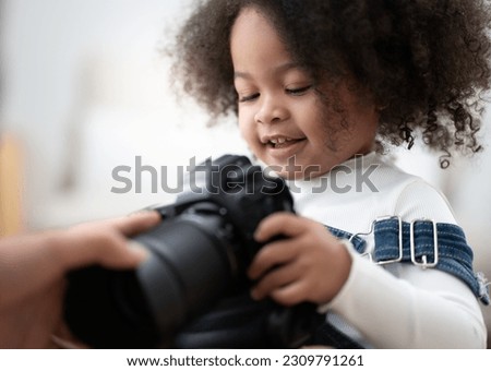 Cute kid playing digital camera learn to take picture. multiracial girl interested in camera and lens to be adorable photographer. Cheerful little child holding equipment with fun, portrait.