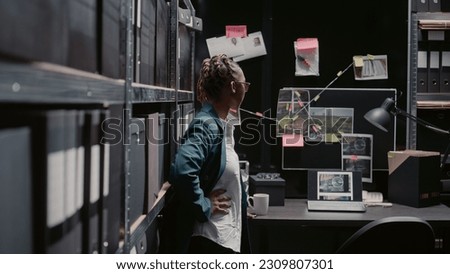 Law enforcement agent checking detective evidence map to find criminal suspect, using board with investigation clues and case files on wall. Policewoman reviewing surveillance photos.