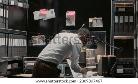 Male inspector examining forensic evidence on map, thinking about solution to solve case. Professional private detective studying clues and criminal records, incident room archive files. Royalty-Free Stock Photo #2309807467