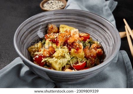 Side view of an Asian salad with shrimps and pineapples in a bowl on a black background, with a textile napkin beside the bowl