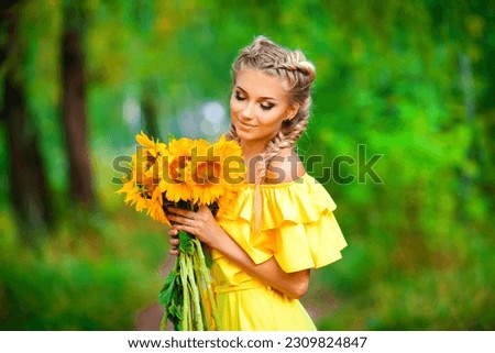 Beautiful young blonde girl in yellow dress enjoying nature. Happy Smiling female standing in green forest with sunflowers. Warm photo. Art work.