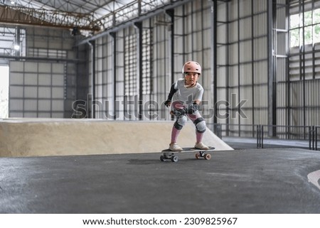 asian child skater or kid girl fun playing skateboard or ride surf skate on pump track and wave bank ramp in school skate park by extreme sports to wearing helmet elbow wrist knee guard body safety Royalty-Free Stock Photo #2309825967