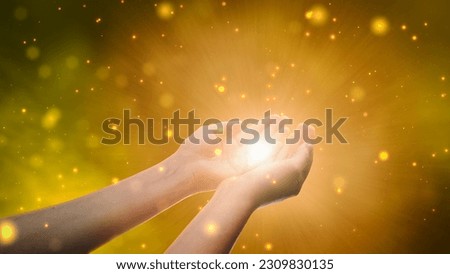 Conceptual Visualization Of Male Or Female Hands Reaching Out In Prayer On Magical Dark Yellow Background. Person Connecting With Higher Spiritual Energy Through Bright Light In Their Palms. Royalty-Free Stock Photo #2309830135
