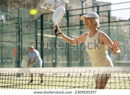 Active aged woman practicing Padel Tennis with other players in the tennis court outdoors Royalty-Free Stock Photo #2309830297