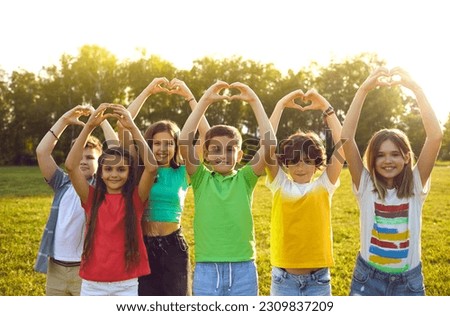 Happy children wish for world peace. Cheerful healthy kids standing on camp field or park lawn in sunset or sunrise sunlight look at camera, smile, raise hands up and do heart gestures. Group portrait Royalty-Free Stock Photo #2309837209