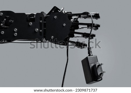 Real robotic hand with AC adapter. Concepts of AI takeover and Technological singularity. Royalty-Free Stock Photo #2309871737