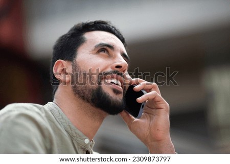 Close up portrait of handsome young middle eastern man talking on small phone outside and looking away