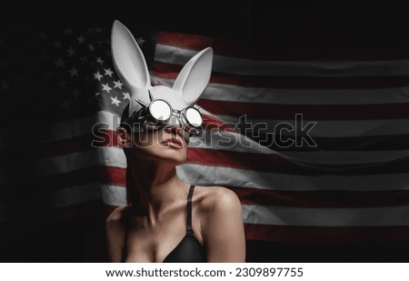young woman in a hare mask against the background of the American flag in steam punk glasses