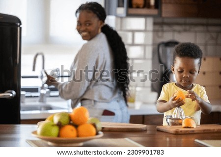 Cheerful African-American mother and son squeezing an orange to make orange juice. Son helping mother in the kitchen and have fun Royalty-Free Stock Photo #2309901783