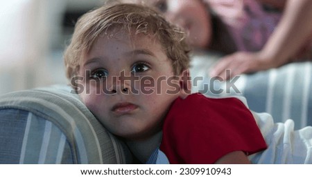 Child watching TV screen while lying on sofa at night