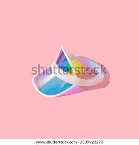 Holographic sports visor hat on sunlight and tennis ball isolated on pink background. Summer vacation recreation, sports accessory, beach visor hat. 80s or 90s lifestyle pattern. Royalty-Free Stock Photo #2309923273