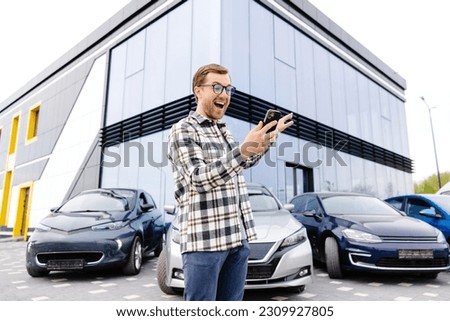 Happy man taking selfie through smart phone after purchasing new car. The man showing the purchased car via video link over the phone.