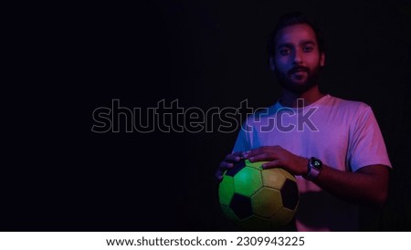 a indian boy with football on black studio background with light red color reflection