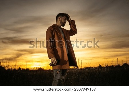 young man drinking coffee in the field with a sunset in the background