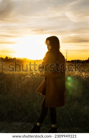 Beautiful woman drinking coffee in a field with sunset in the background