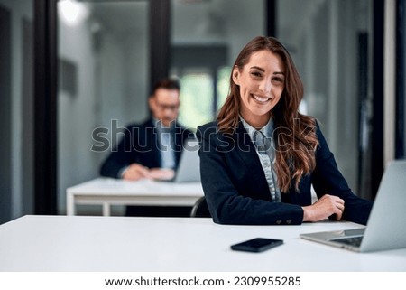 A happy female employee sitting at the office table and working on a laptop and smiling for the camera. Royalty-Free Stock Photo #2309955285