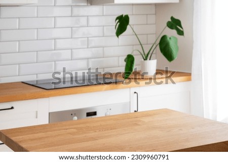 Wooden tabletop with free space for product montage or mockup against blurred white kitchen with cutting board and plant in scandinavian style in morning light Royalty-Free Stock Photo #2309960791