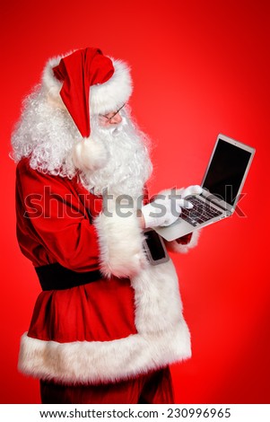 Modern Santa Claus using laptop computer over red background. Christmas.