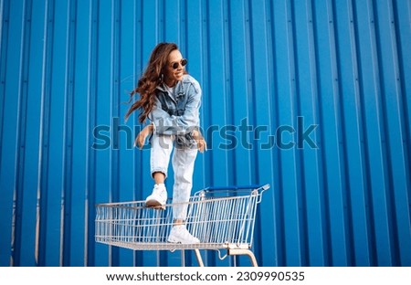 Young woman with shopping cart having fun near color wall. smilling african woman going shopping. 
