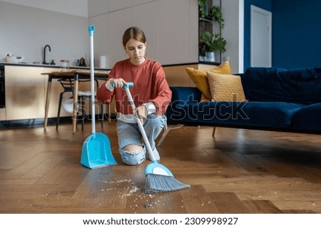 Teen girl doing simple household chores, sweeping floor with broom in living room while helping parents in cleaning house. Teenager child tidying up, keeping home clean Royalty-Free Stock Photo #2309998927