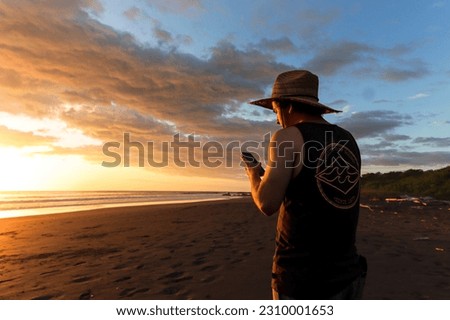 Image of a traveler on the beach of Tamarindo watching the orange and purple sunset meditating, taking pictures and enjoying the sound of the sea and the warmth of the sunset in Costa Rica.