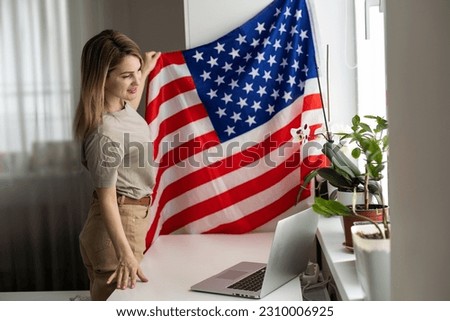 Picture of happy young lady with USA flag using laptop computer. Looking camera.