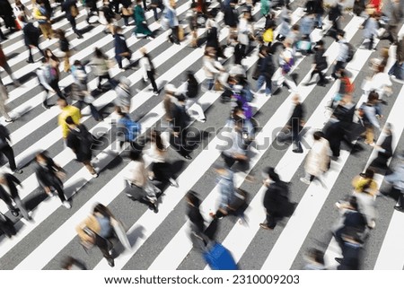 picture with intentional motion blur of crowds of people who are crossing a city street at a zebra crossing in Tokyo, Japan