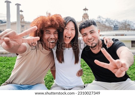 Group of friends gesturing the peace sign looking at camera and smiling together. Three multiracial teenages having fun showing the victory fingers. Positive cheerful high school students laughing
