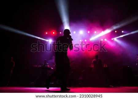 Silhouette of a man singing during a concert with lights flashing in background.