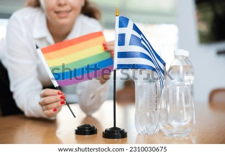 Young female assistant setting up greek and rainbow flags for international negotiations