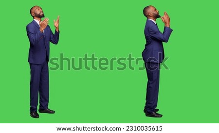 Spiritual office worker praying to god for luck on camera, wearing business suit over full body greenscreen. Corporate employee holding hands in a prayer, religious man with beliefs.