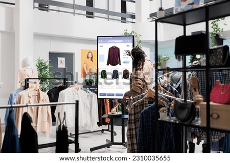 African american man looks at clothes online on touch screen monitor in fashion boutique at mall, self service board. Male customer looking for trendy clothes and items on retail kiosk display. Royalty-Free Stock Photo #2310035655