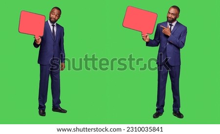 Young entrepreneur showing empty speech bubble, using blank isolated copyapce for advertisement on camera. Office worker in suit using red icon billboard for ad on green screen backdrop.