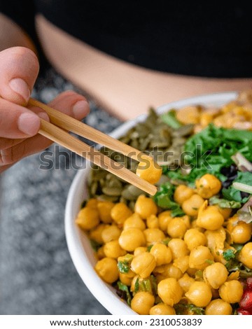 Salad bowl in disposable plate with chickpeas, seeds and seaweeds eating with chopsticks. Closeup. Royalty-Free Stock Photo #2310053839