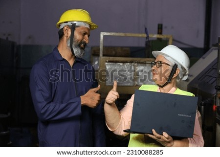 Indian happy senior engineer working on laptop in factory with worker in factory