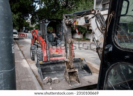 Photo shows a small red excavator on a construction site.