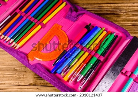Different school stationeries (pens, pencils, ruler and protractor) in pink pencil box