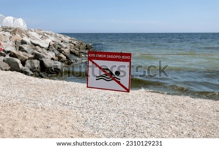 bright red "No Swimming" sign on city's sea sandy beach in Odessa during Russia's attack on Ukraine. Swimming is prohibited! Approaching the water is prohibited. War. Mortal danger to life during war