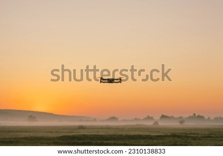 silhouette of a flying drone in a field at sunset.