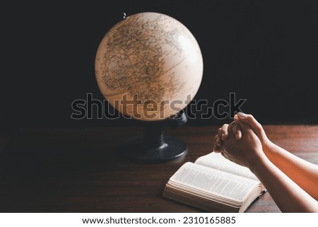 Christian woman praying for globe and people around the world on wooden table with bible. Christian hands praying together around a wooden table with bible page in homeroom.