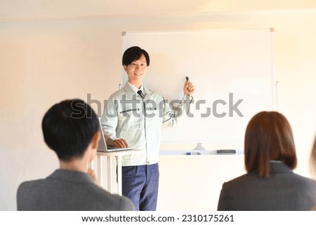 A male worker giving a presentation and multiple business people attending
