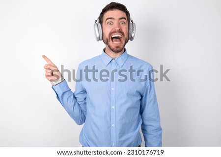 business man wearing blue t-shirt with headphones over white background points aside on copy blank space. People promotion and advertising concept