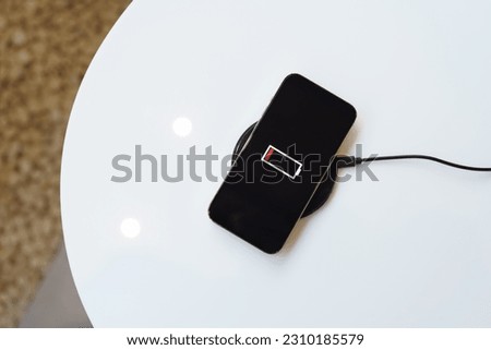 Charging mobile phone battery with wireless charging device in the table. Smartphone charging on a charging pad. Mobile phone near wireless charger Modern lifestyle technology concept Royalty-Free Stock Photo #2310185579