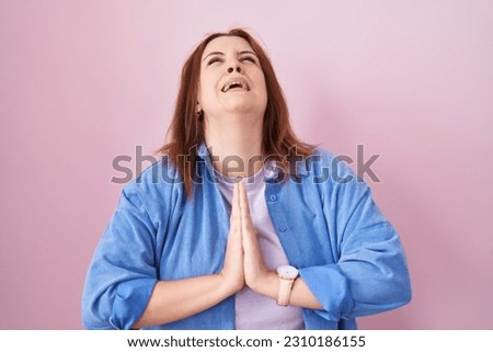 Young hispanic woman with red hair standing over pink background begging and praying with hands together with hope expression on face very emotional and worried. begging.  Royalty-Free Stock Photo #2310186155