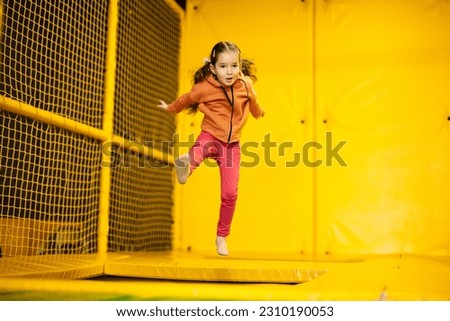Little girl kid jumping on trampoline at yellow playground park. Child in motion during active entertaiments. Royalty-Free Stock Photo #2310190053