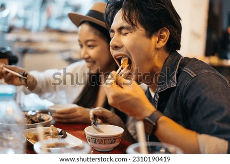Young Asian couple traveler tourists eating Thai street food together in China town night market in Bangkok in Thailand - people traveling enjoying food culture concept Royalty-Free Stock Photo #2310190419